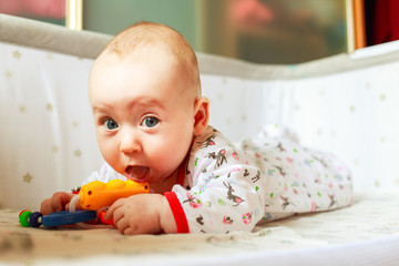Четырех месячный ребенок играет у себя в кроватке дама. Ребенок грызет игрушки 