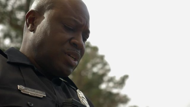 An African American police officer talks with someone as he looks down at a notebook.