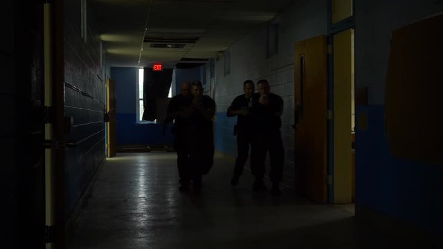 A Squad Of SWAT Team Police Walk In A School With Guns Drawn To Train For Responding To School Shootings.