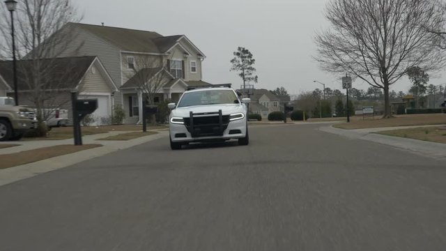A police squad car drives through a suburban neighborhood while on patrol.
