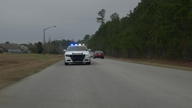 A police squad car drives with its blue lights flashing to pull over another car.