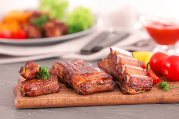 Wooden board with delicious grilled ribs on table