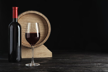 Glass, bottle and barrel with delicious red wine on table against dark background