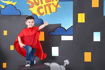 Cute boy in superhero costume against comic strip themed decoration
