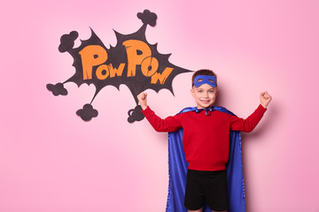 Cute boy in superhero costume on color background