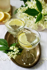 A cool drink with lemon and elderflower syrup in glasses on a metal tray. Rustic style.