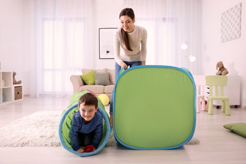 Nanny and little boys playing with toy tunnel at home