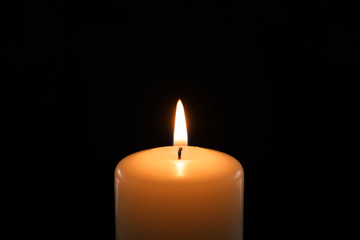 Wax candle burning on black background, closeup
