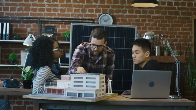 Bearded man in glasses showing miniature of manufacture and explaining principle of alternative energy resources usage to team