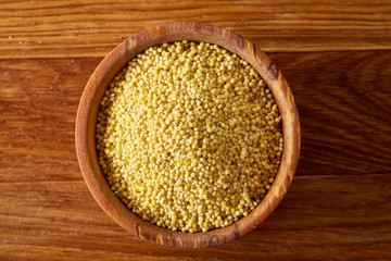 Millet in a wooden bowl on rustic wooden background, top view, close-up, selective focus.