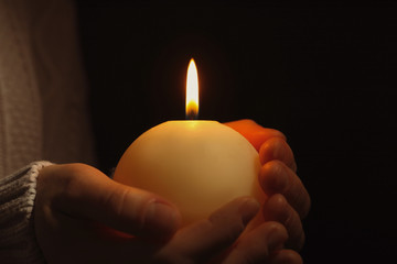 Young person holding burning candle in darkness, closeup