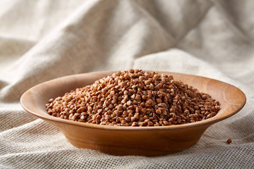 Close-up buckwheat in a round wooden plate over homespun tablecloth, top view, selective focus.