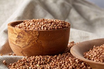 Bowl and plate full of buckwheat grains on homespun tablecloth, close-up, selective focus, shallow depth of field.