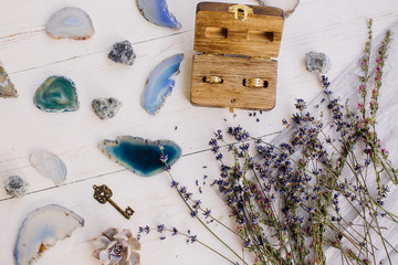 lavender, blue and turquoise stones, key and wooden casket with wedding rings on a white wooden background