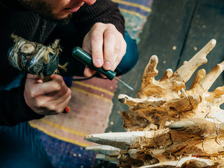 A man master woodcarver creates a sculpture of wood with a chisel and hammer