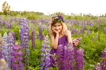 Beautiful girl smiling in a violet dress with a wreath of lupines