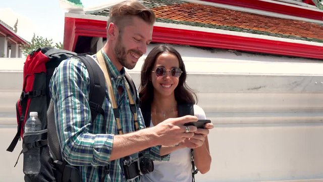 Lovely young tourist couple taking selfie with smartphone at Thai temple while traveling on summer holidays in Bangkok, Thailand