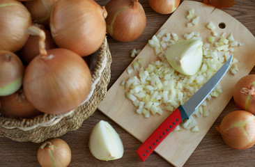 Onions in a basket and on a cutting board. Many onion bulbs in a wicker basket. Vegetables sliced on a cutting board. View from above.