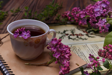 Beautiful violet lilac flowers with white cup with coffee or tea, on a wooden background