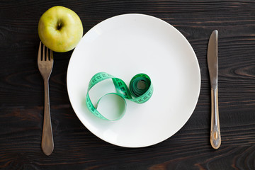Losing weight. Strict diet. Empty plate and measuring tape instead food on wooden background top view mockup