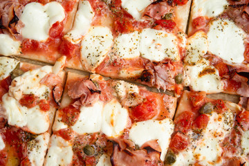 Homemade pizza with ham, mozzarella, tomato sauce, capers and oregano 