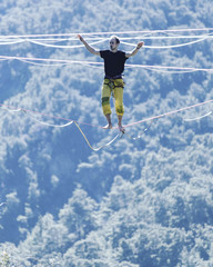 Fototapeta na wymiar Highliner on a rope. Highline on a background of mountains. Extreme sport on the nature. Balancing on the sling. Equilibrium at altitude.