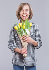 Beautiful girl with bunch of flowers on gray background. Smiling child with bouquet of yellow tulips as a gift. Happy mothers, Birthday or Valentines day.