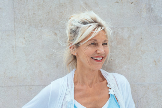 Blonde mature smiling woman against bright wall