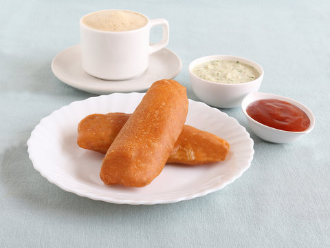 Raw banana bajji or fritter, a popular Indian vegetarian snack, with coconut chutney and tomato ketchup as side dishes and filter coffee.