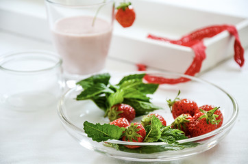 Whole fresh ripe strawberries with peppermint leaves on glass plate. Making refreshing summer drinks.