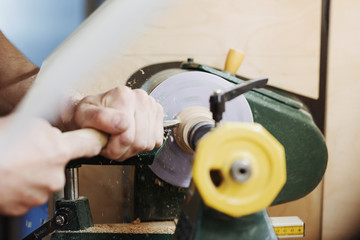 Unrecognizable man's hands hold chisel near lathe, joiner working at small wood carpenter. An artisan carves a piece of wood using a manual lathe