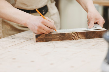 Carpenter marking a measurement on a wooden plank. Working weekdays in workshop of joiner