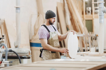 Portrait view of concentrated motivated  bearded hardworking middle aged professional male carpenter worker looking and choosing wood in the workshop or fabric