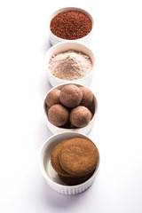 Nachni / Ragi laddu and biscuits or cookies made using  finger millet, sugar and ghee. It's a healthy food from India. Served in a bowl or plate with raw whole and powder. Selective focus