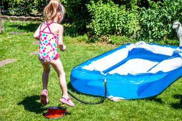Little girl jumping on the bellows to blow up inflatable swimming pool