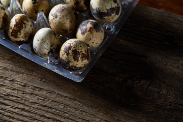 Quail eggs in a plastic container on a dark wooden background, top view, selective focus, shallow depth of field