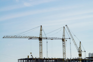 Fototapeta premium Big tower cranes above buildings under construction against blue sky. Background image of construction close-up with copy space. Build of city.