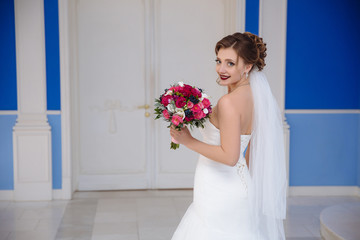 View from the back of the bride smiling turns around in front of the entrance to the ceremony hall. The girl looks very happy, shows her beautiful pink bouquet.