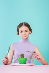 stylish female teenager eating cactus with fork and knife, diet concept