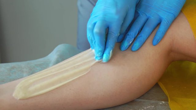 Close-up of the hand in rubber gloves is applied to the hair removal paste and by special technology shugaring removes hair