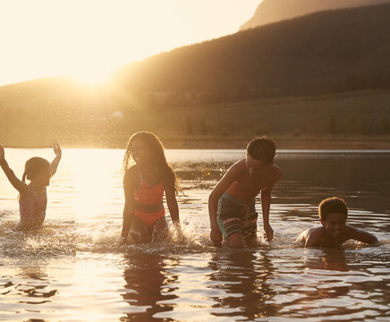 Children With Friends Enjoying Evening Swim In Countryside Lake