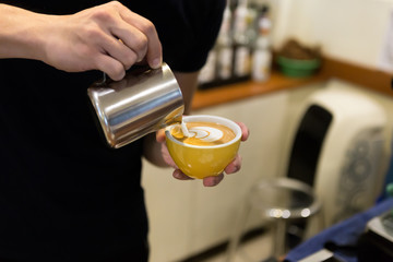 Barista man pouring cream into glass with coffee.