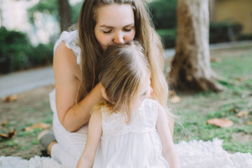 Portrait of happy beautiful young mother kissing her adorable little daughter, family picnic at summer
