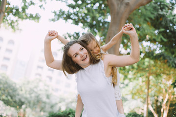 Beautiful young woman her little daughter having fun doing piggyback in summer park