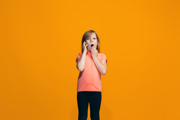 The happy teen girl standing and smiling against orange background.