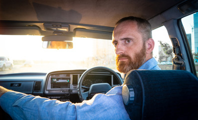 A bearded man driving an old car in the rays of the setting sun. Portrait.