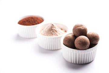 Nachni laddu or Ragi laddoo or balls made using  finger millet, sugar and ghee. It's a healthy food from India. Served in a bowl or plate with raw whole and powder. Selective focus