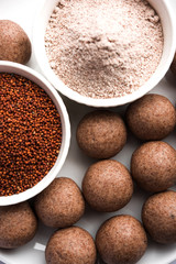 Nachni laddu or Ragi laddoo or balls made using  finger millet, sugar and ghee. It's a healthy food from India. Served in a bowl or plate with raw whole and powder. Selective focus