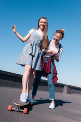 low angle view of smiling woman teaching her female friend riding on skateboard