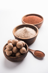 Nachni laddu or Ragi laddoo or balls made using  finger millet, sugar and ghee. It's a healthy food from India. Served in a bowl or plate with raw whole and powder. Selective focus